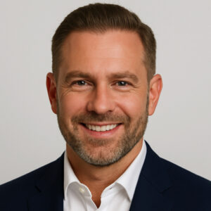 Headshot of Derek Langford in a navy blue blazer and white button-up shirt. He is smiling warmly against a plain light gray backdrop.