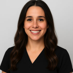 Portrait of Marissa Delgado with long, dark brown hair styled in soft waves, wearing a black V-neck scrub top. She is smiling confidently in front of a neutral light gray background.